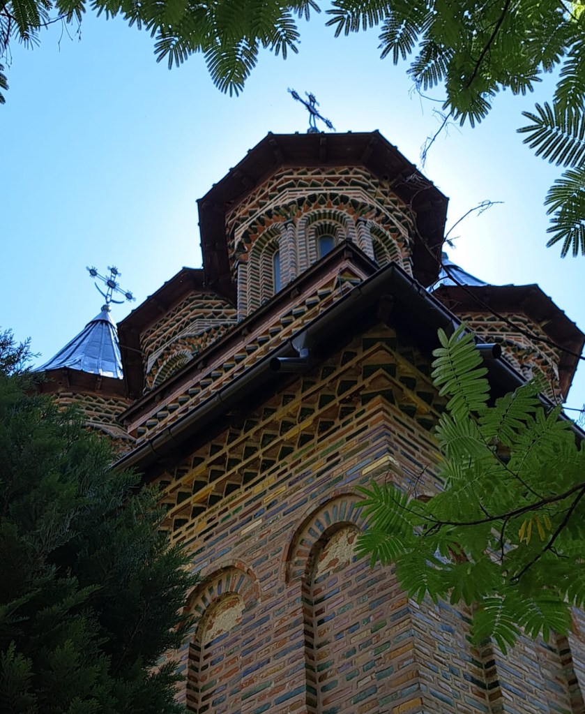 View of a brick church with intricate patterns and domes, partially obscured by trees.