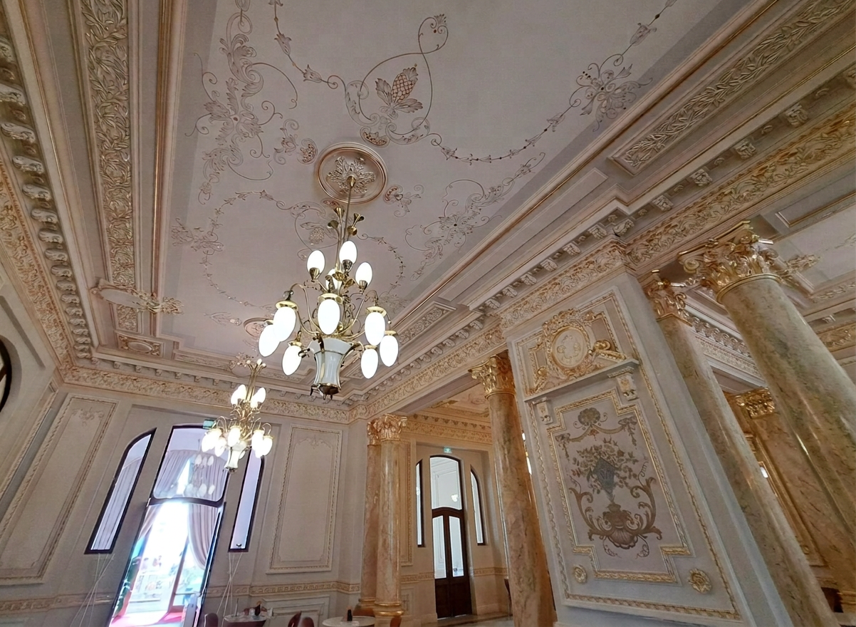 WhatsApp Image 2026-09-08 at 22.06.33 (25) Interior view of a lavishly decorated room featuring ornate ceiling details, elegant chandeliers, and marble columns.