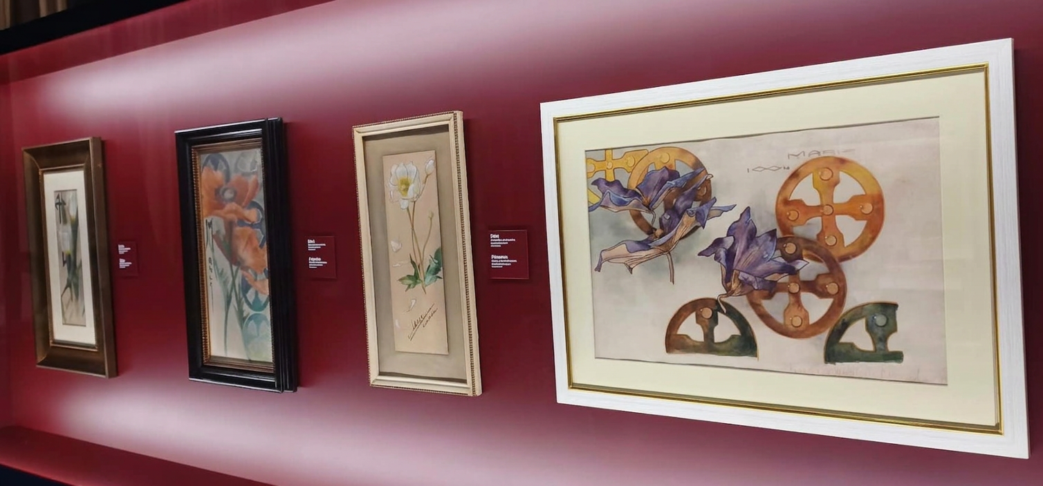 WhatsApp Image 2026-09-08 at 22.06.33 (16) A gallery wall displaying four framed artworks, featuring floral designs and abstract motifs, against a deep red background.