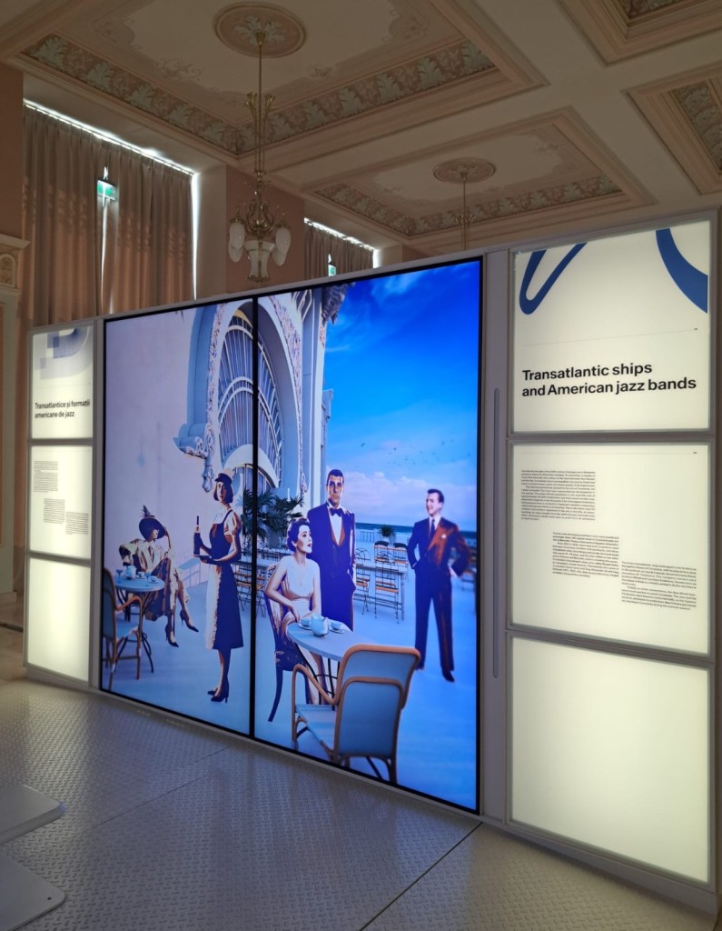Exhibit showcasing a colorful display about transatlantic ships and American jazz bands, featuring people in vintage attire enjoying a café setting with an ocean view.