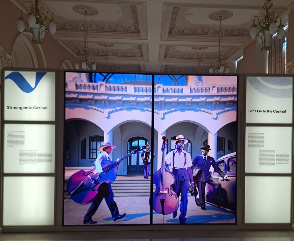 A digital display featuring musicians in period attire, walking towards a historic building, with a sign that reads 'Let's Go to the Casino!'