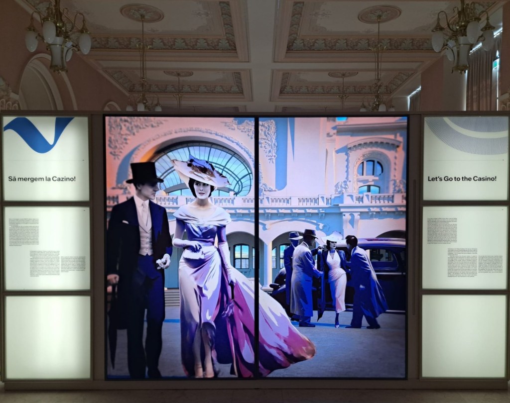 An exhibition display featuring vintage-styled images of a couple in elegant attire walking toward a casino, alongside scenes of people interacting near a car, with decorative architecture in the background.
