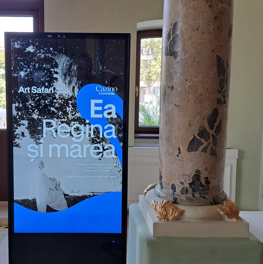Digital display for 'Art Safari' exhibition titled 'Ea Regina și marea', showcasing event details and dates, located near a decorative stone column.